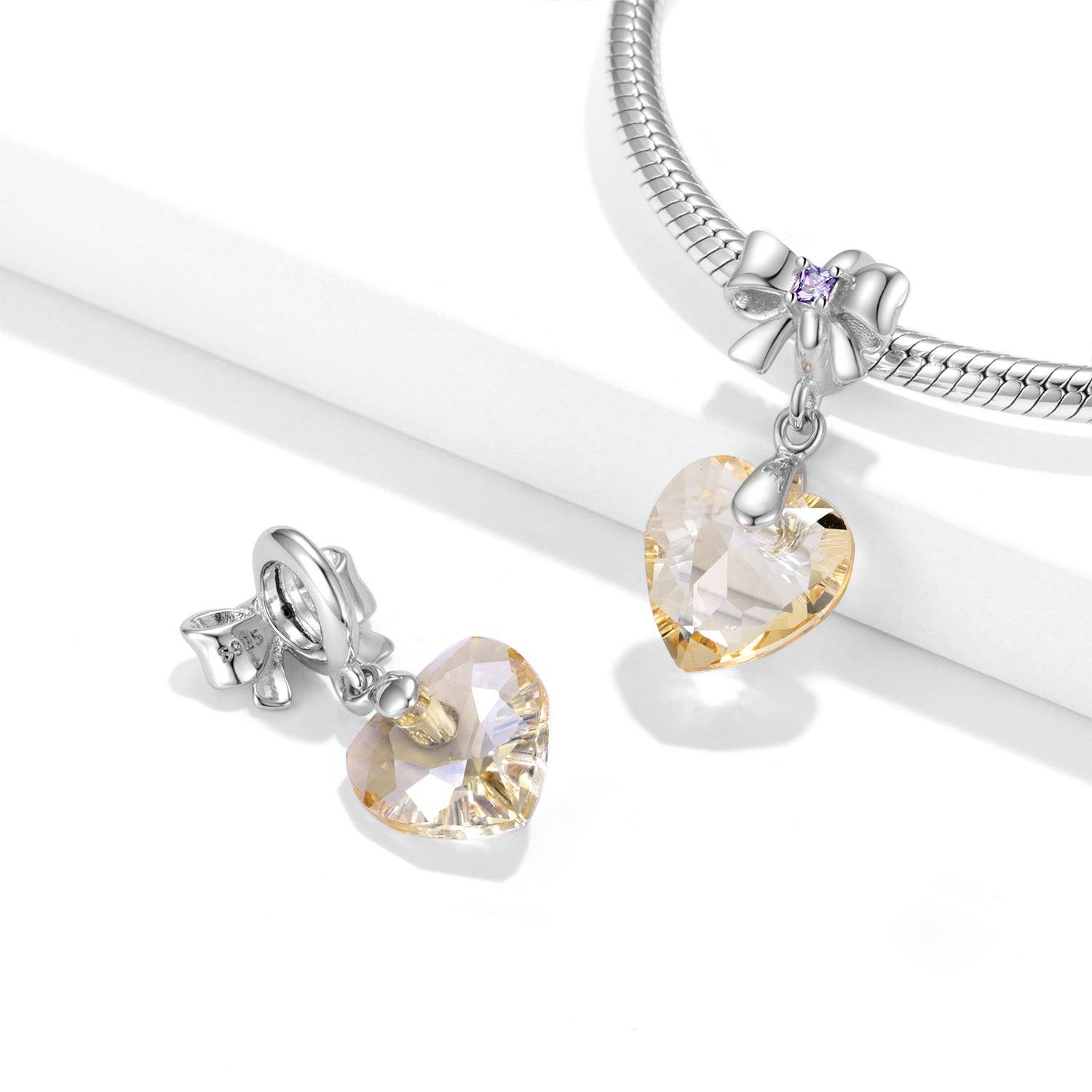 Elegant Golden Crystal Charm displayed on a silver bracelet, featuring a heart-shaped gemstone and bow detail. Ideal for jewelry lovers.