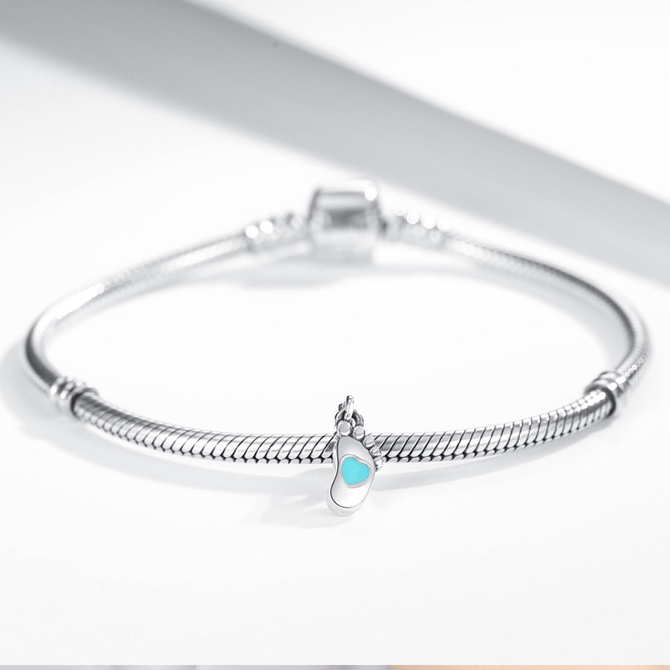 Baby footprint charm attached to a sterling silver bracelet, featuring a turquoise heart detail. A meaningful jewelry piece for parents.