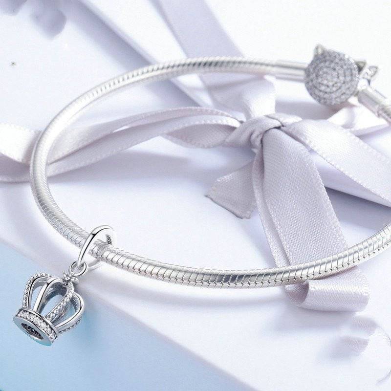 Silver bracelet with crown dangle charm and ribbon detail.